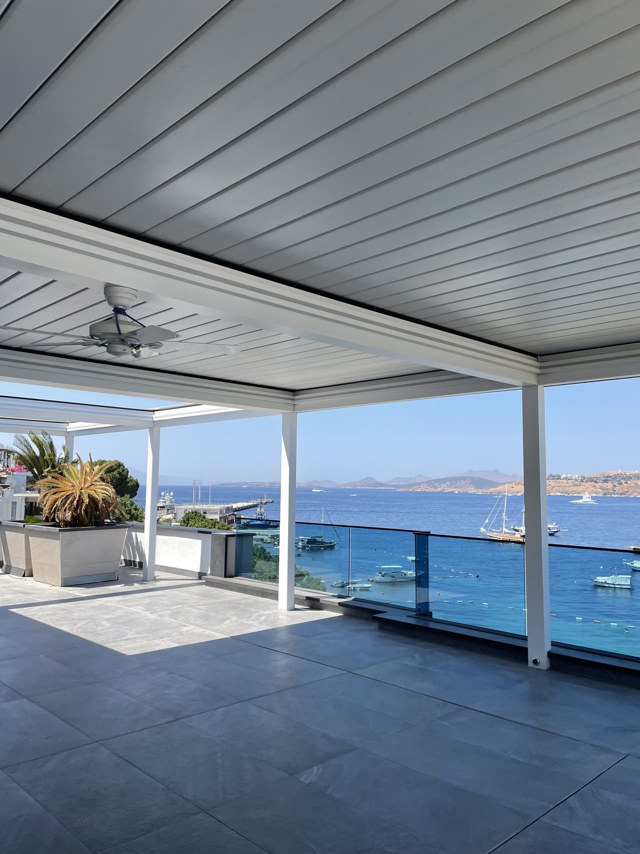 White louvered roof with ceiling fan on a seaside terrace